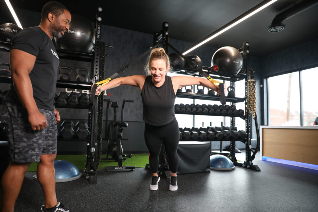 Male personal trainer coaching a female client in the gym on the TRX machine